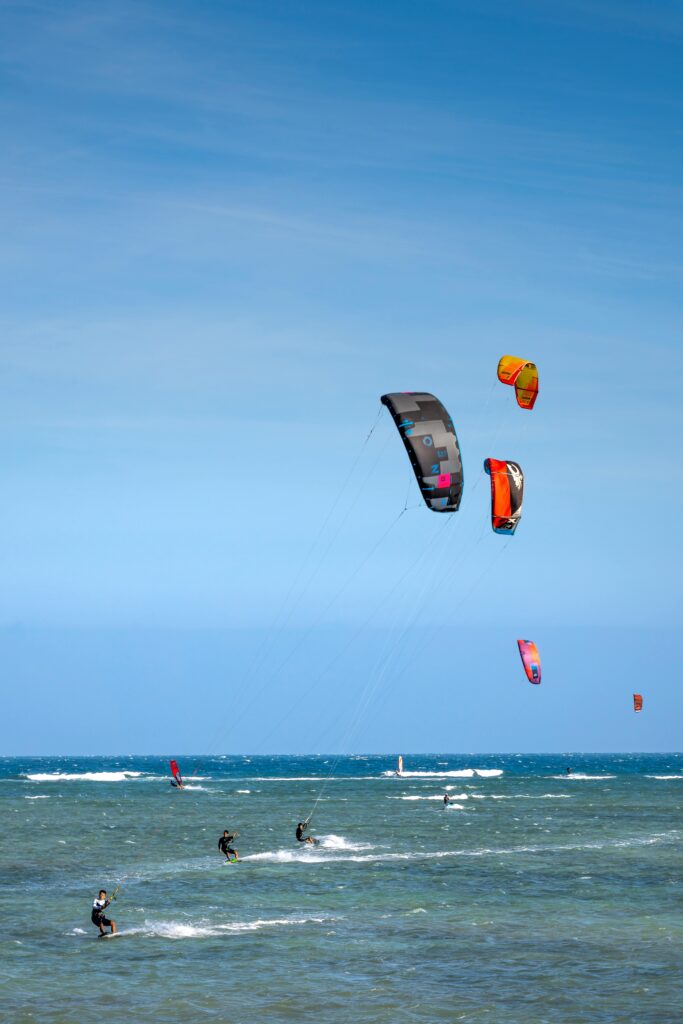 Anonymous kiteboarders with power kites practicing extreme sport on wavy sea under cloudy blue sky in daylight